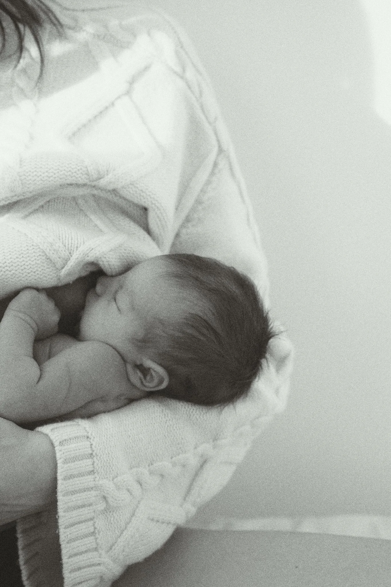 A newborn baby swaddled in a white knitted blanket, sleeping peacefully.