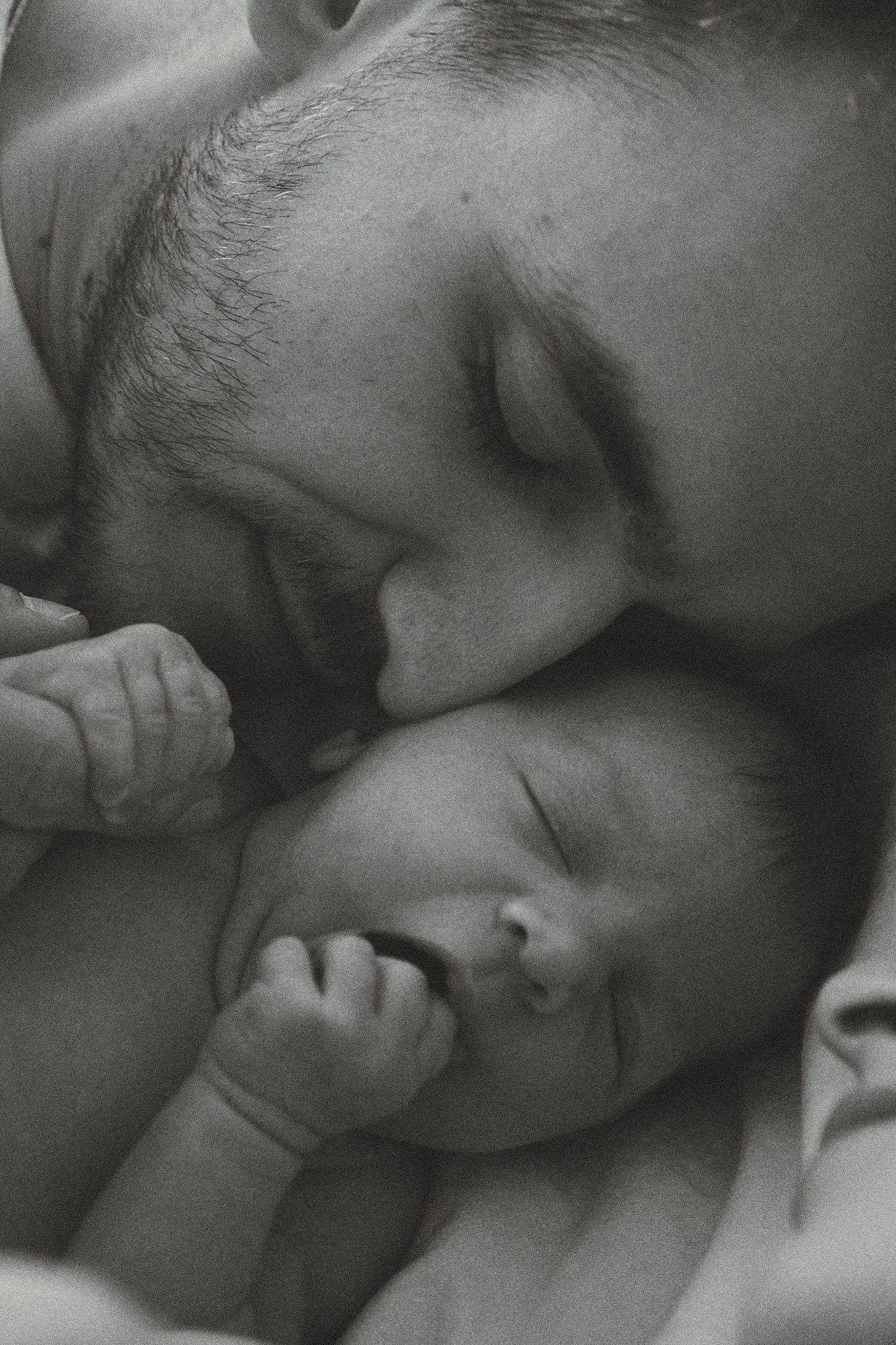 Close-up of a newborn baby sleeping next to an adult, who is gently touching the baby's head.