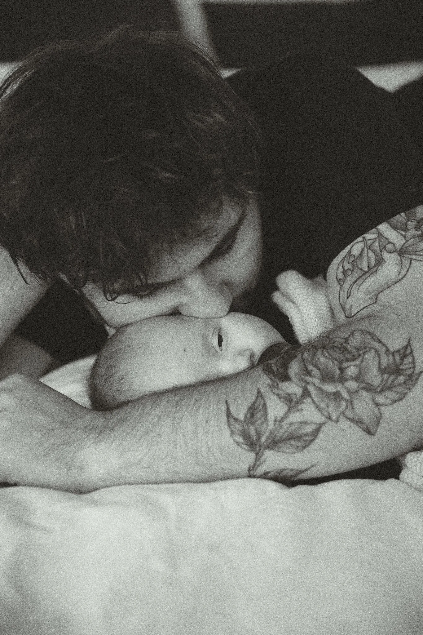 Close-up of a person with tattoos embracing and kissing a baby on the forehead, captured in a tender moment.