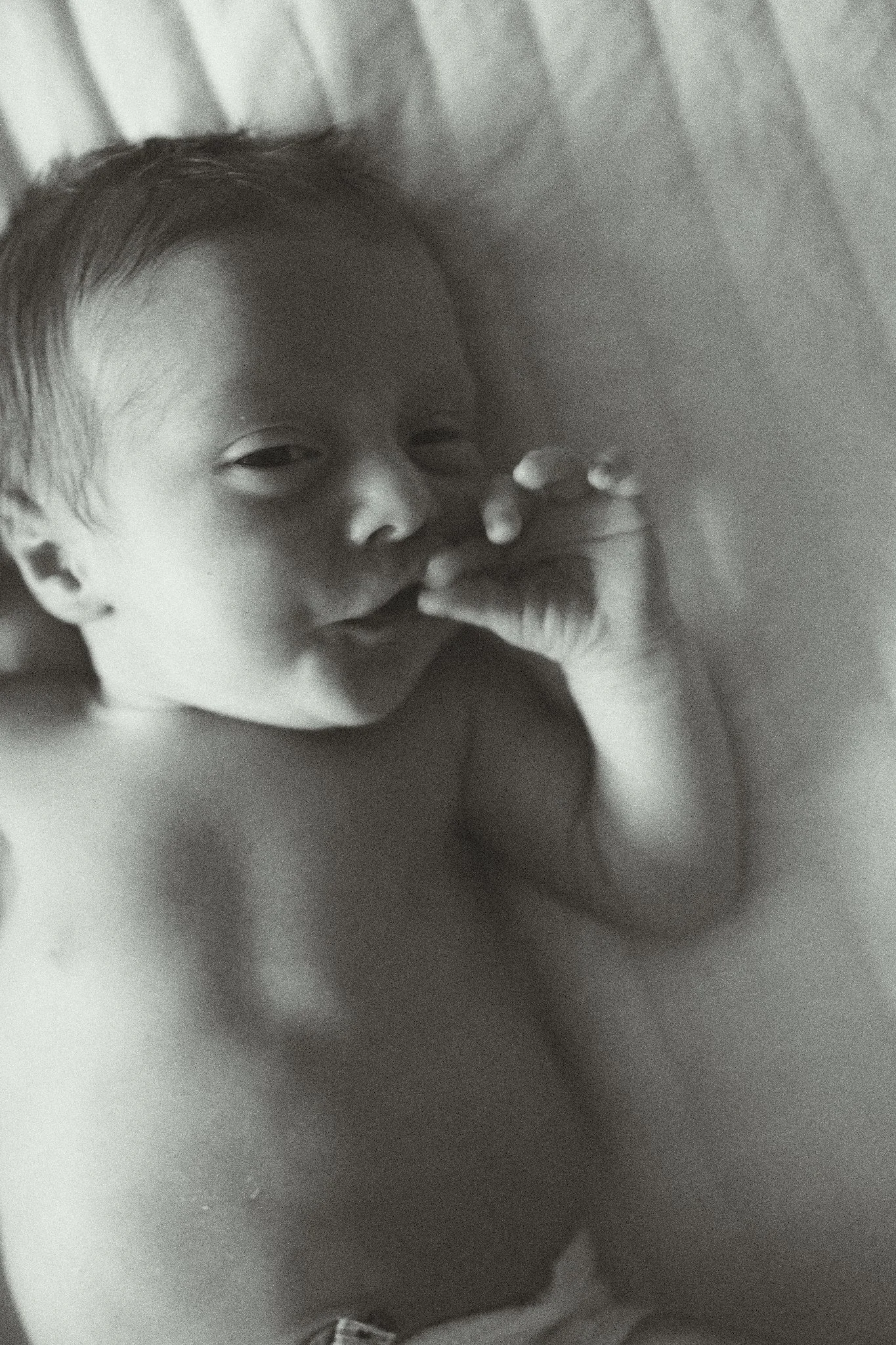 Black and white photo of a newborn baby sucking its thumb.