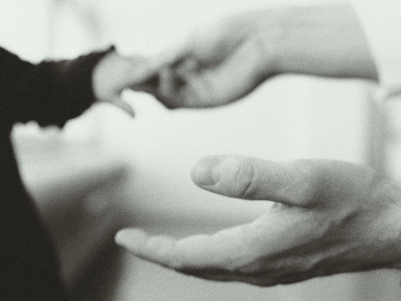 Blurred black and white image of two hands reaching towards each other.
