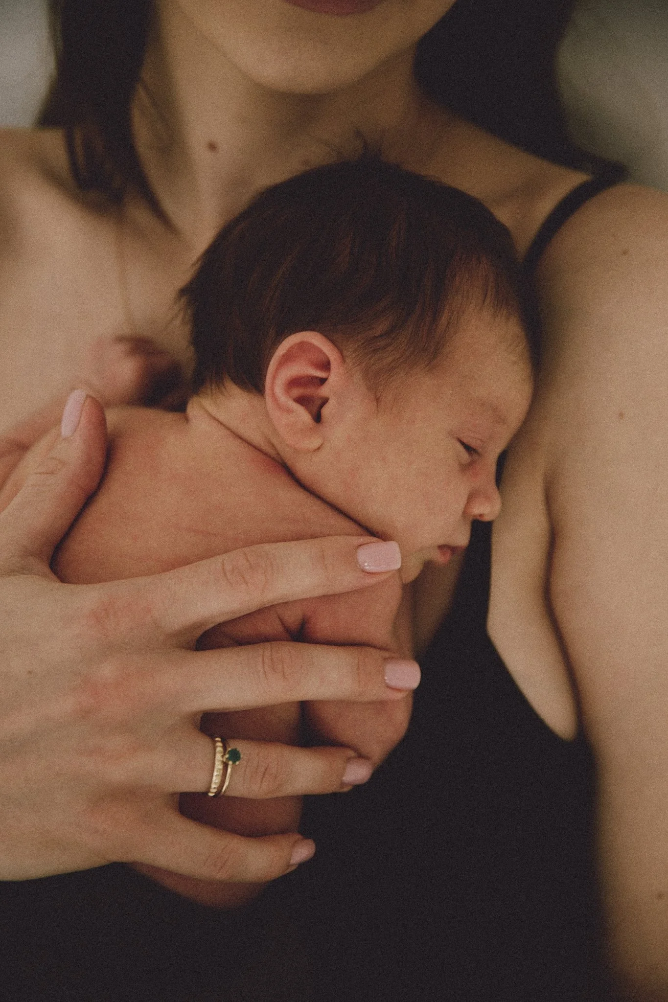 Newborn baby sleeping on woman's chest, close-up of mother's hand with ring.