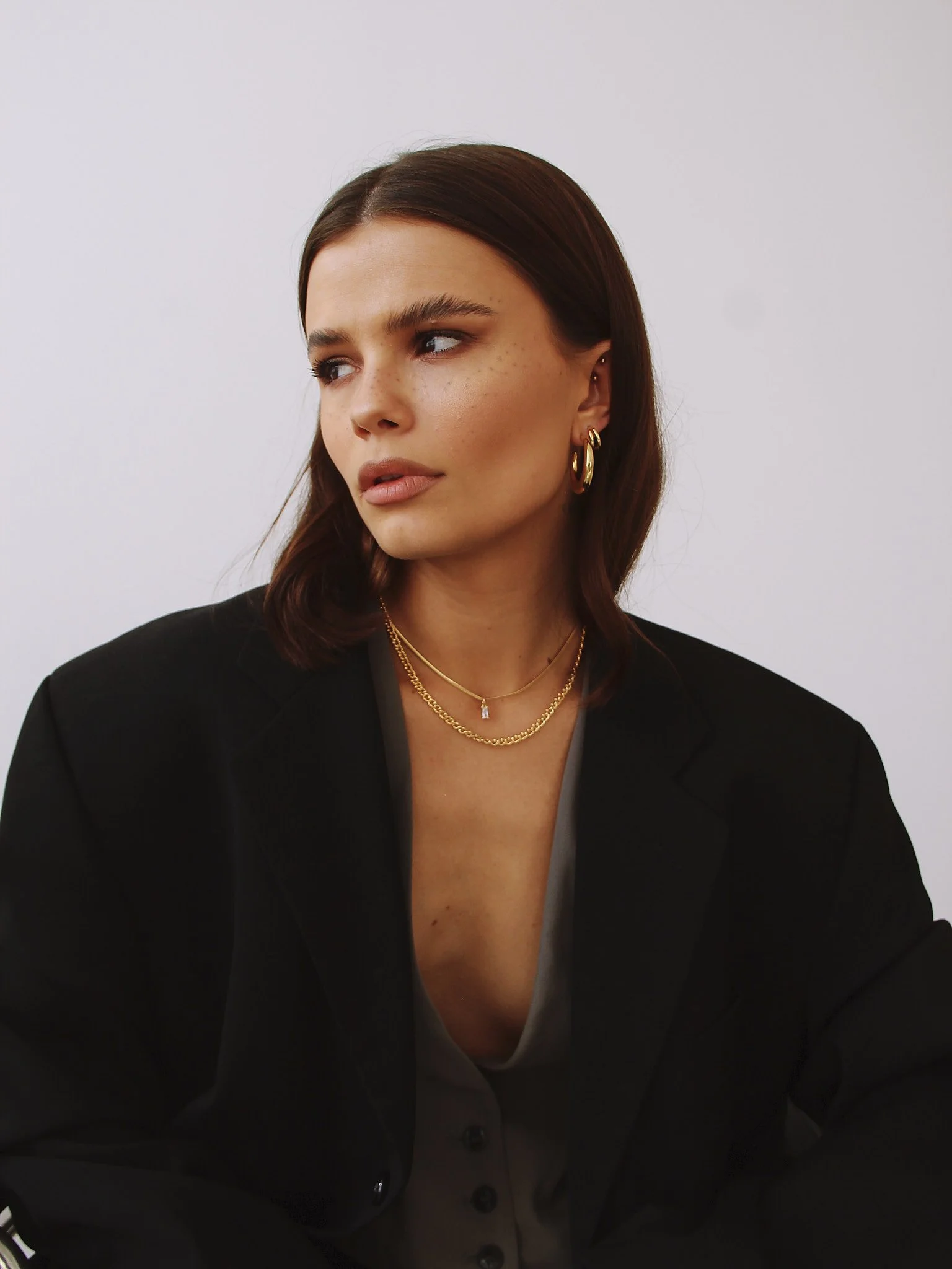 Woman with brown hair wearing a black blazer and gold hoop earrings