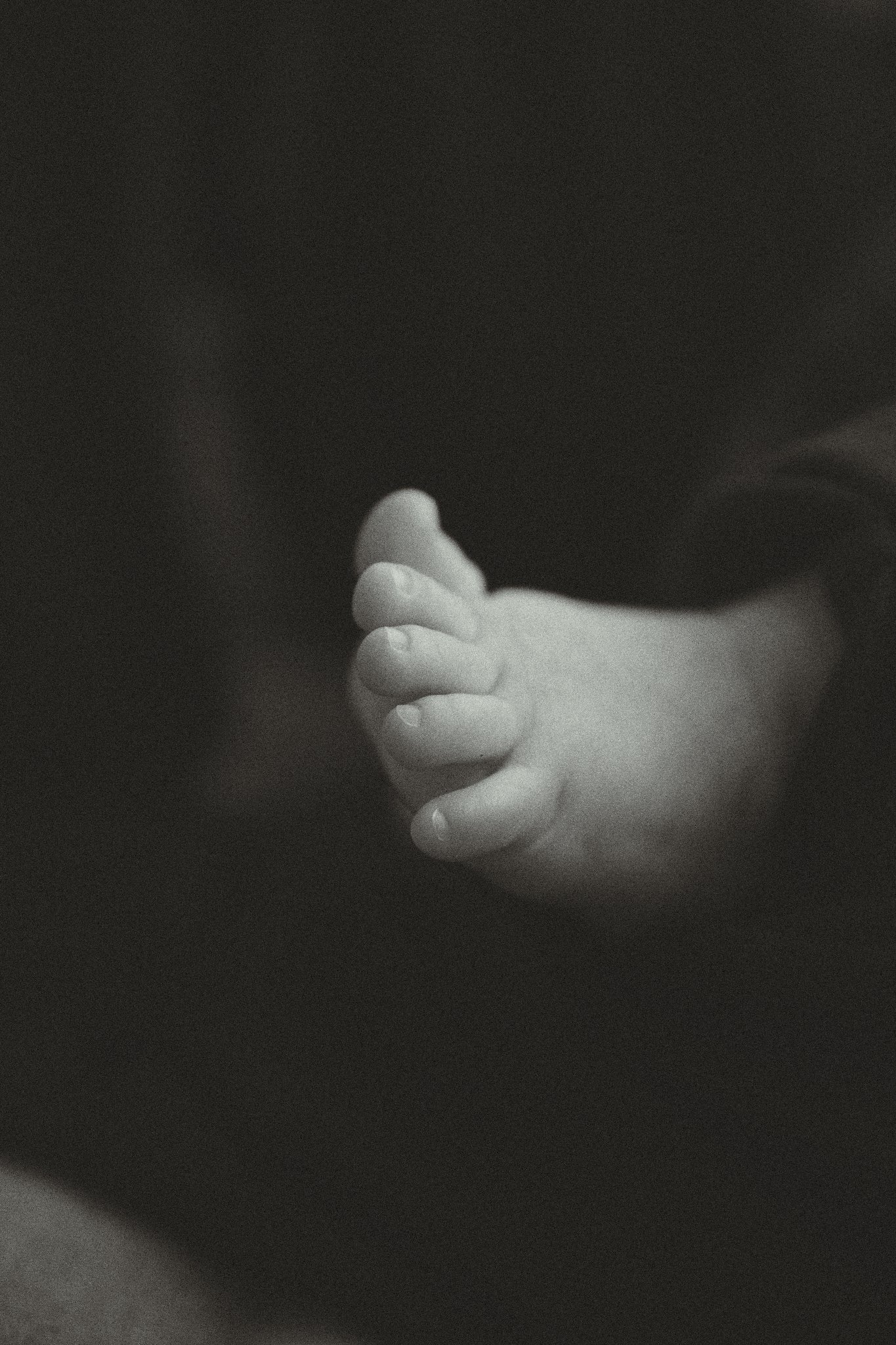 Close-up of a baby's foot with focus on the toes against a dark background.