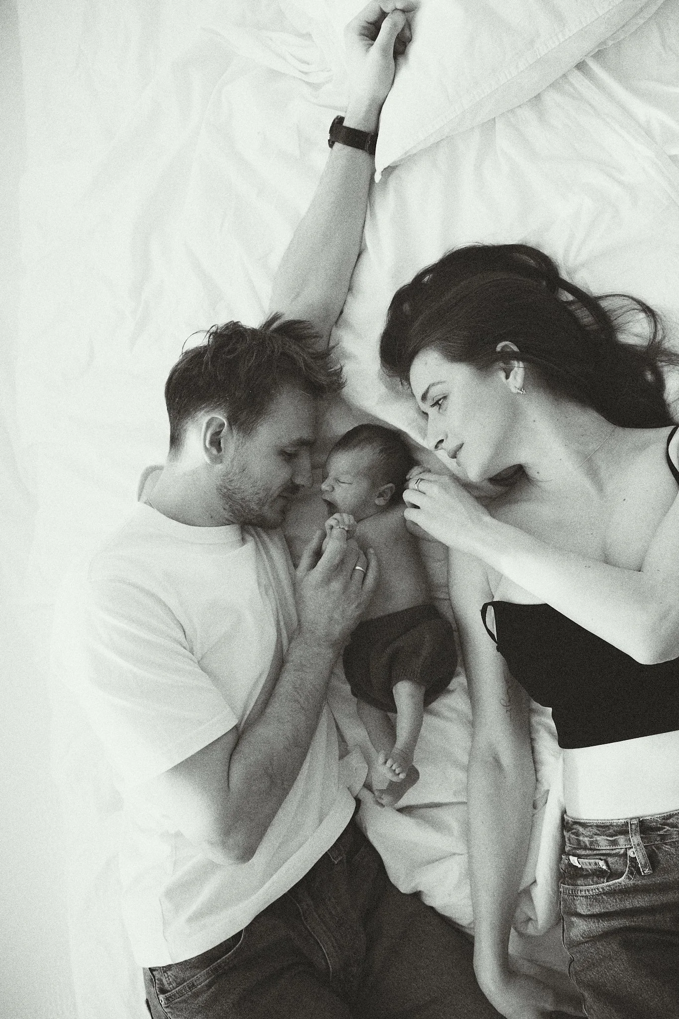A man and woman lying in bed with a newborn baby between them, in a black and white photo.