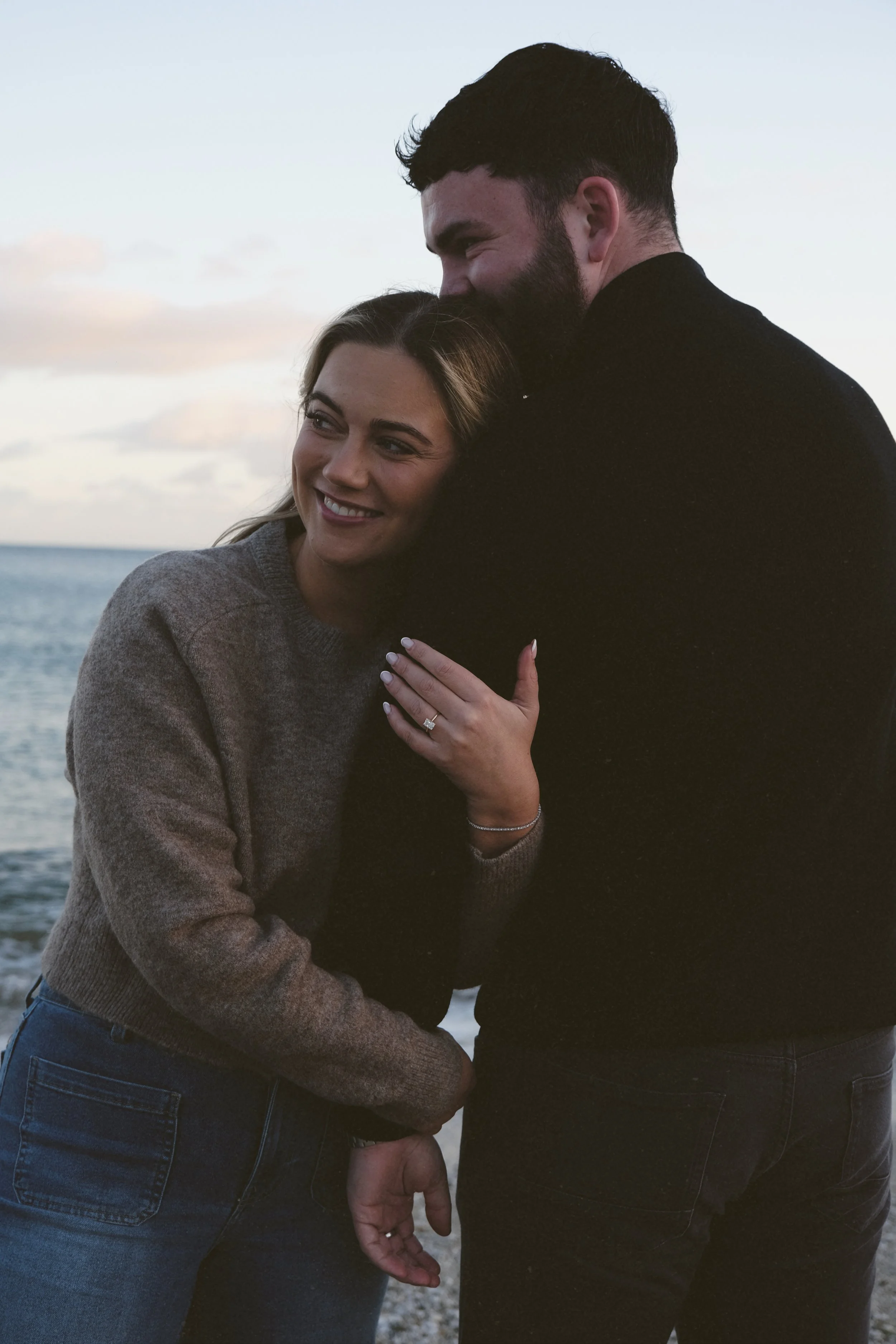 couples engagement shoot shows woman holding the mans arm looking off into the distance beautiful engagement ring 