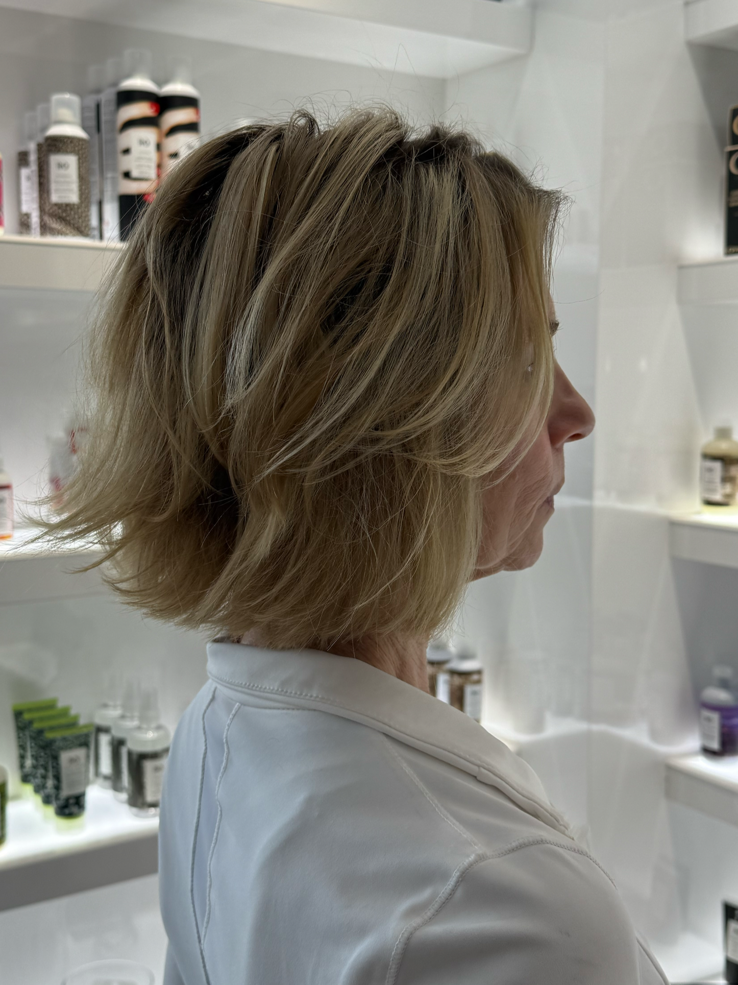 A person with blonde hair shopping in a store aisle with shelves displaying cosmetic and skincare products such as bottles and boxes.