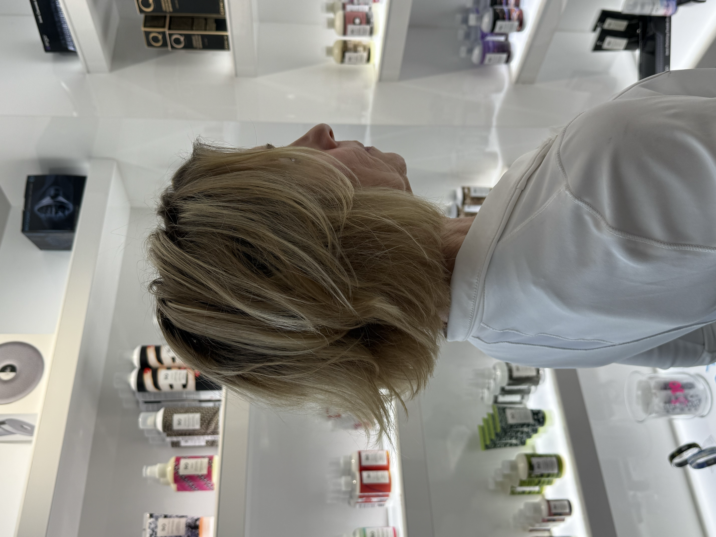 A person with blonde hair shopping in a store aisle with shelves displaying cosmetic and skincare products such as bottles and boxes.
