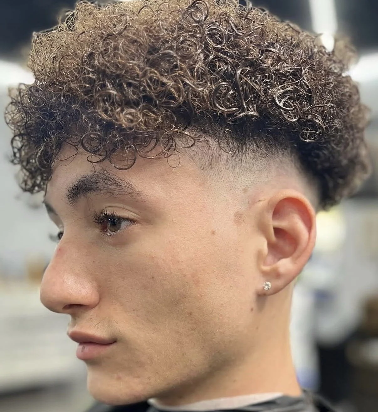 Close-up profile of a young woman with short curly hair and a fade haircut, wearing a small earring.