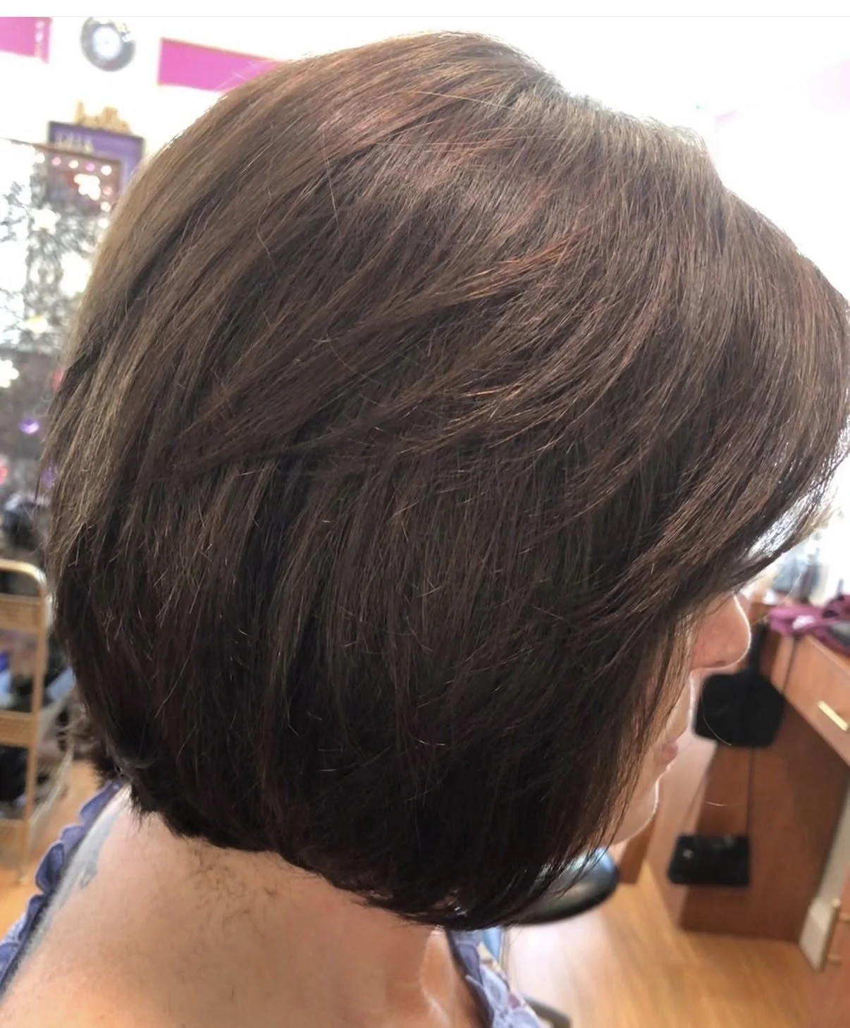 Woman with a short, layered brunette hairstyle, viewed from the side indoors.