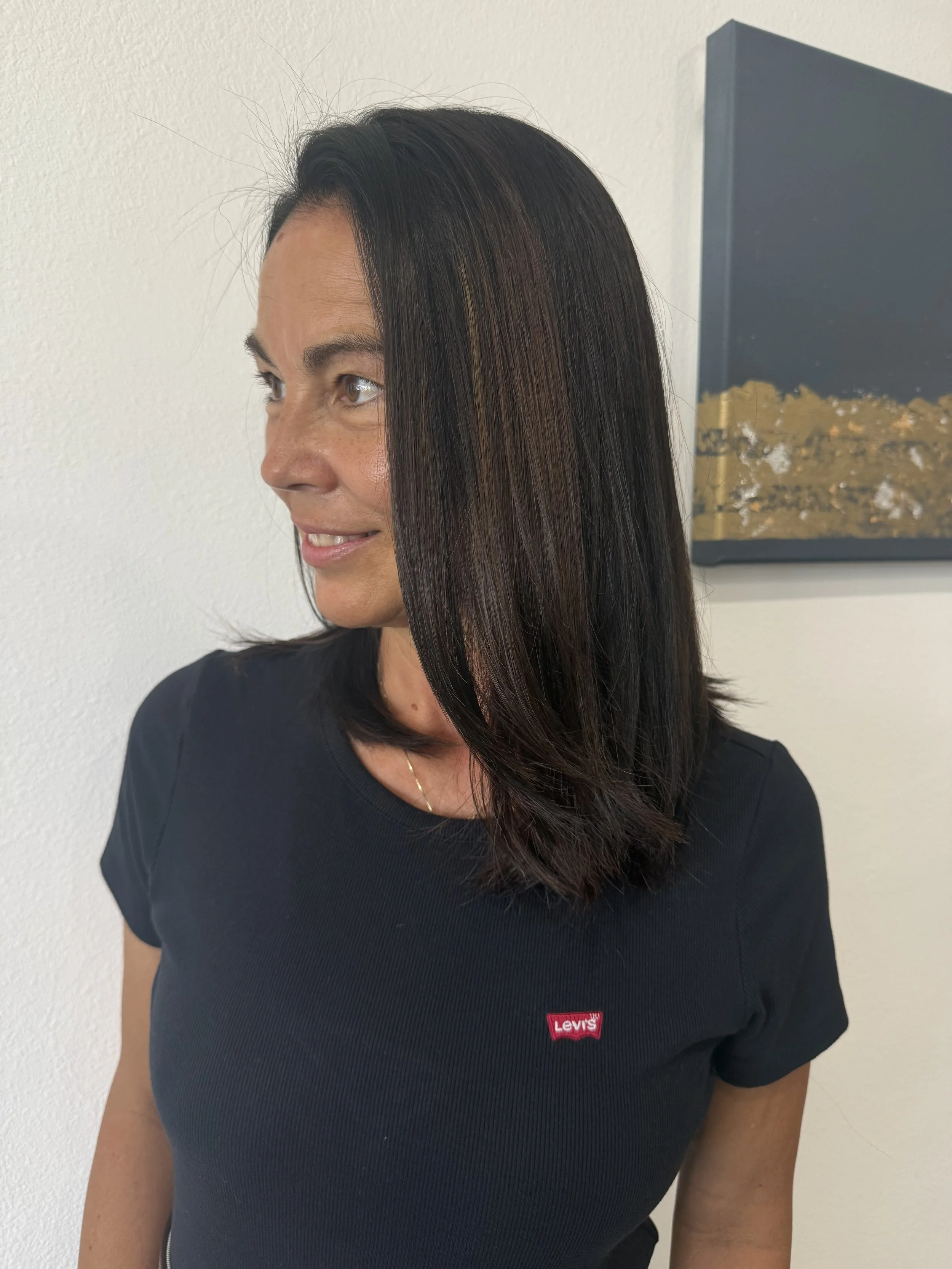 A woman with straight dark brown hair and a black Levi's t-shirt standing against a white wall.