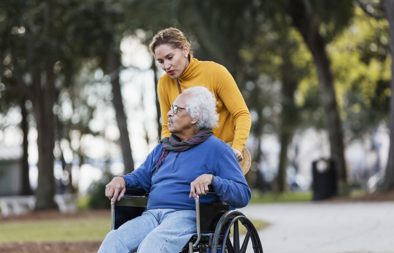 A woman pushing an elderly man in a wheelchair in a park.