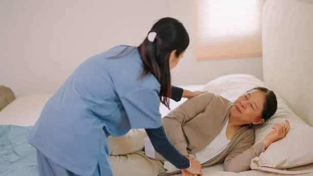 A nurse tending to an elderly woman lying in bed in a bedroom.
