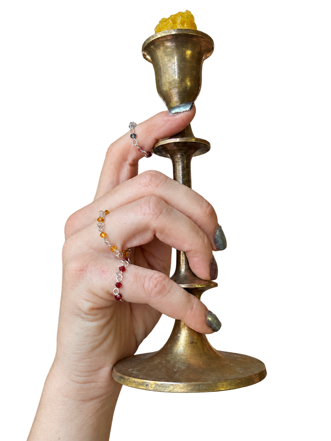 A hand wearing several Vampire’s Kiss rings holds a vintage silver candlestick.