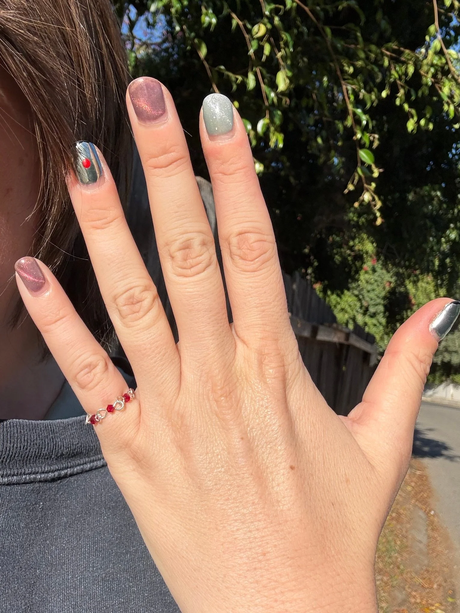 Burgundy Vampire’s Kiss ring worn on a little finger outdoors in sunlight, with metallic nail polish.