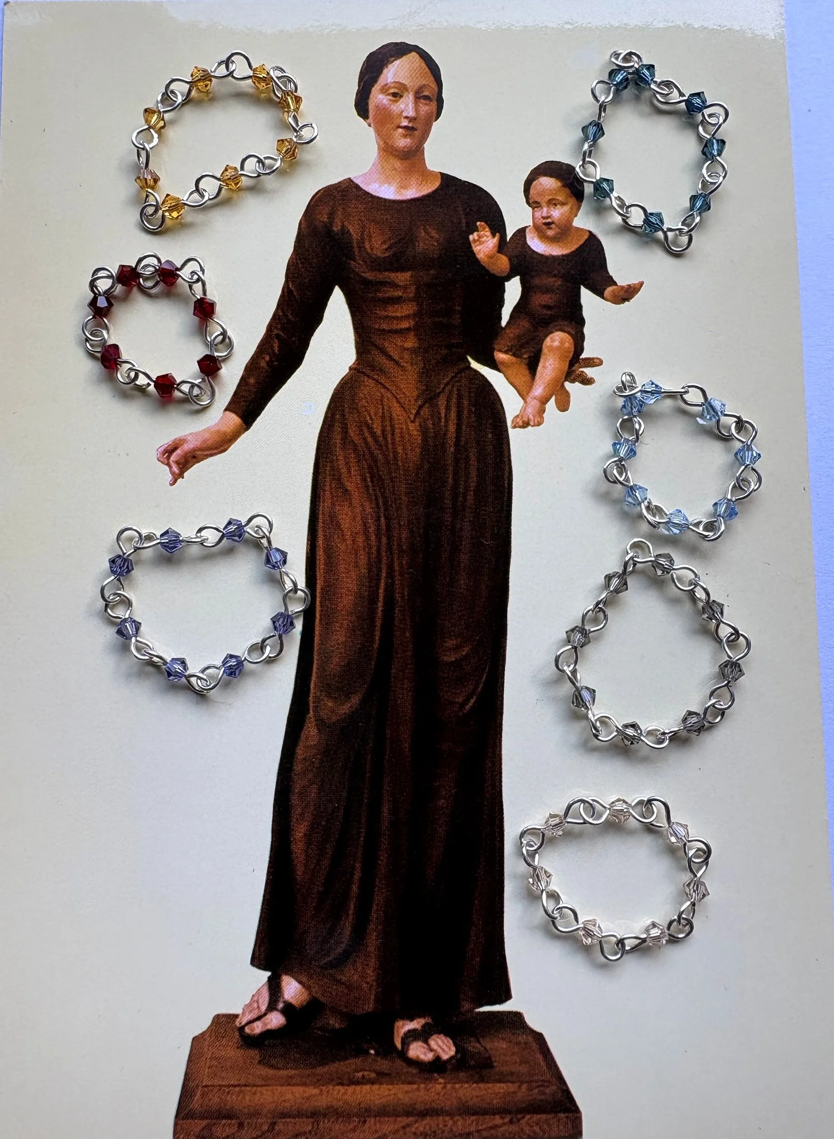 Seven Vampire’s Kiss rings arranged around a vintage mother-and-child devotional card.