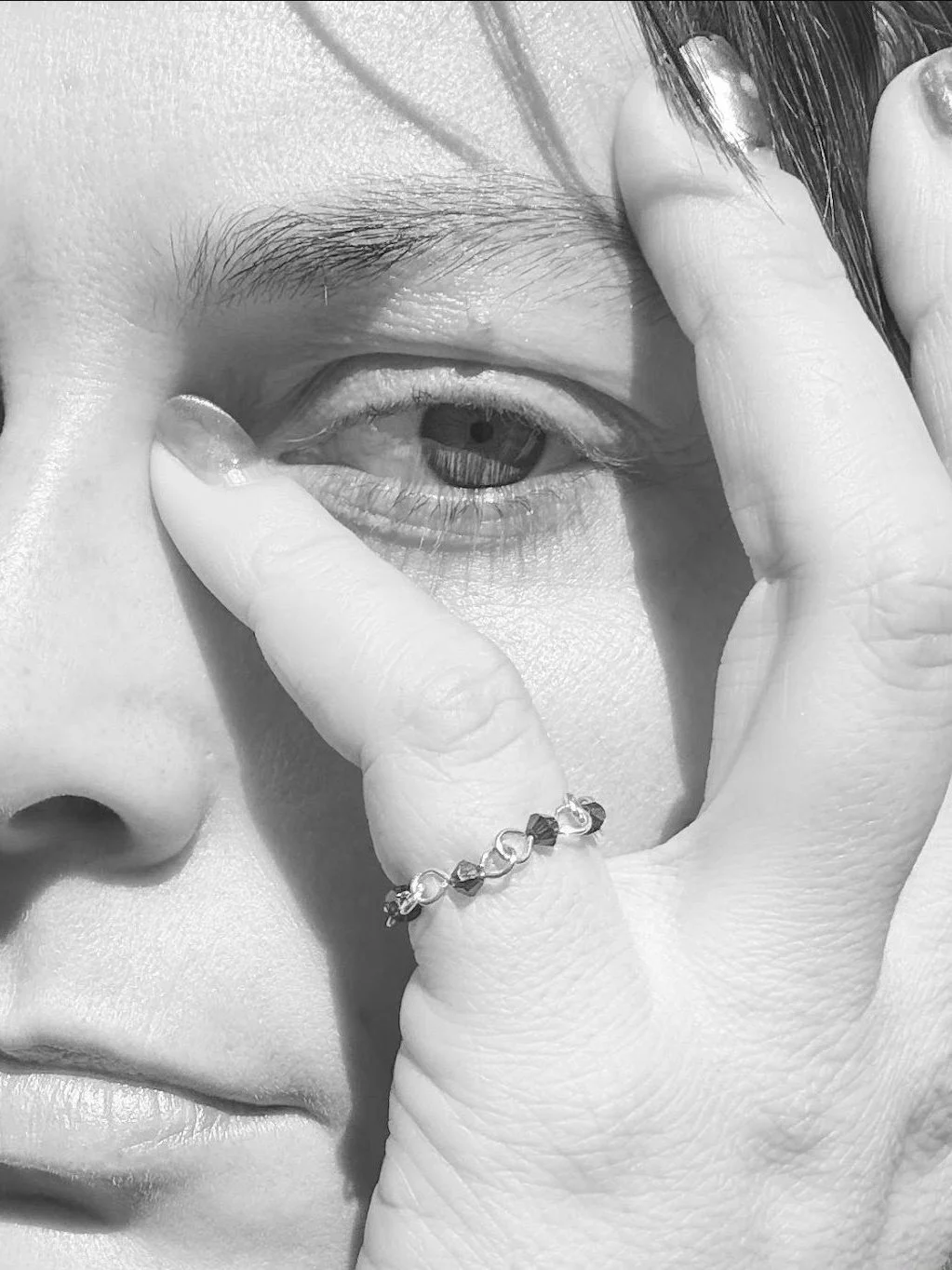 Black-and-white close-up portrait with a Vampire’s Kiss ring worn on the hand beside the eye.