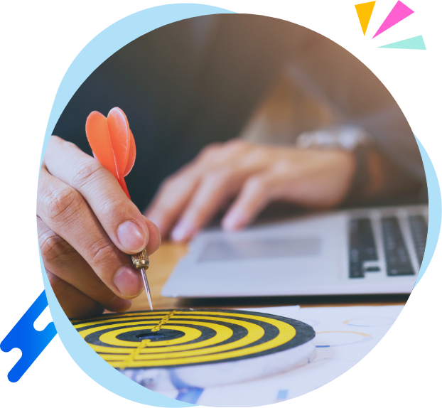 Person holding a dart and aiming at a yellow and black target on a table, with a laptop nearby.