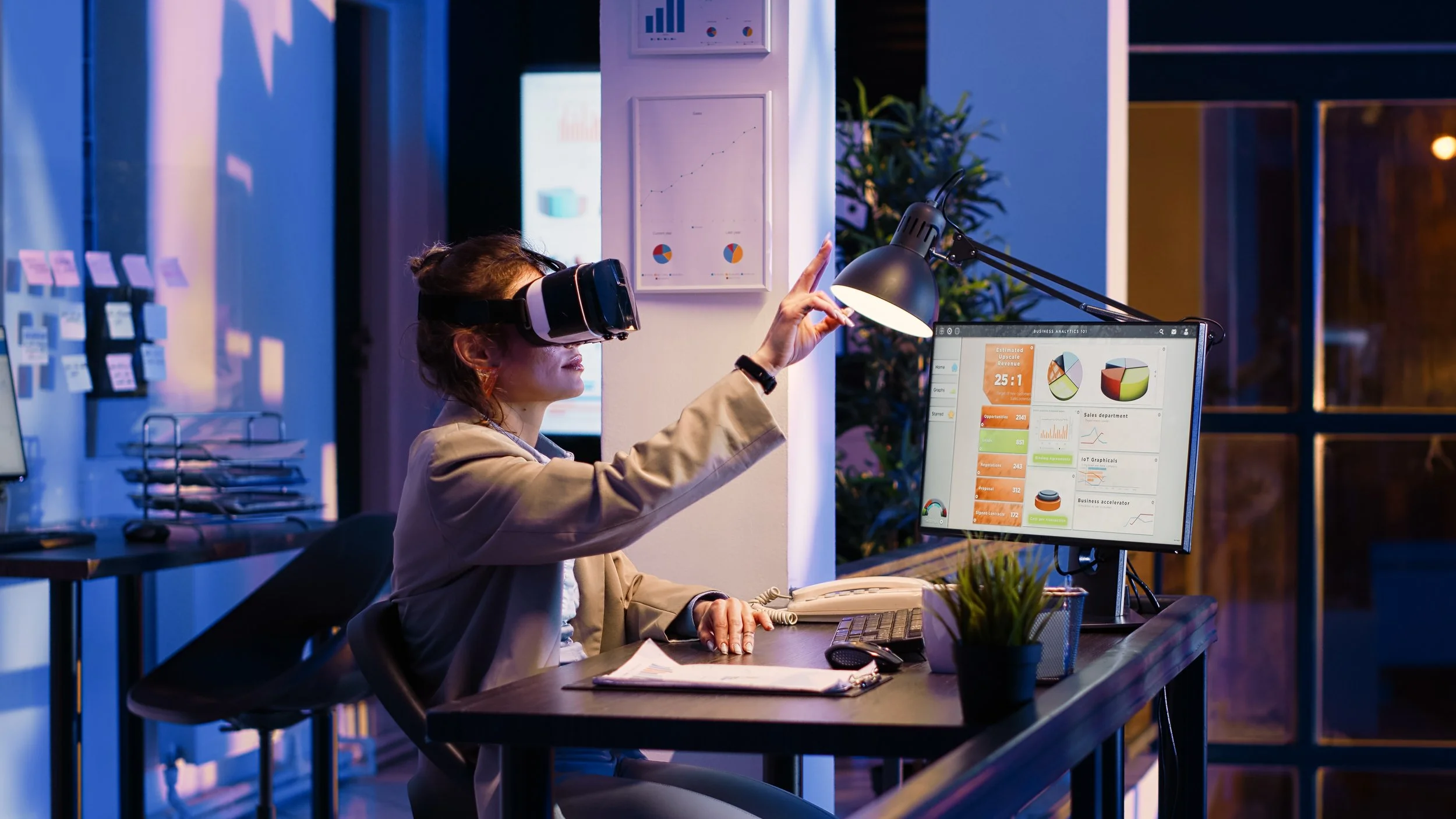 Woman wearing a virtual reality headset and sitting at a desk with multiple computer screens in a modern office environment