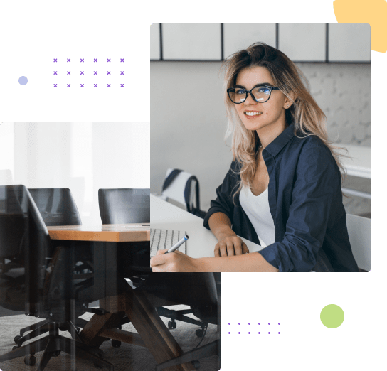 A young woman with glasses sitting at a desk in a modern office, smiling at the camera, with a laptop in front of her.