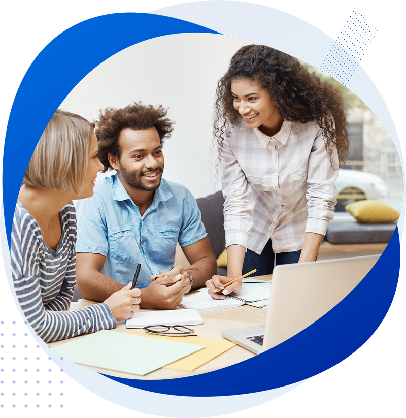 Group of three diverse young adults working together at a table with a laptop, notebooks, and pens in a bright modern office.