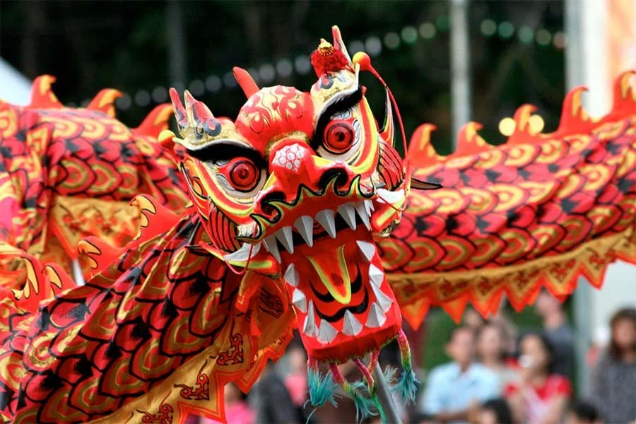 Colorful Chinese dragon lantern in a parade with people watching in the background.