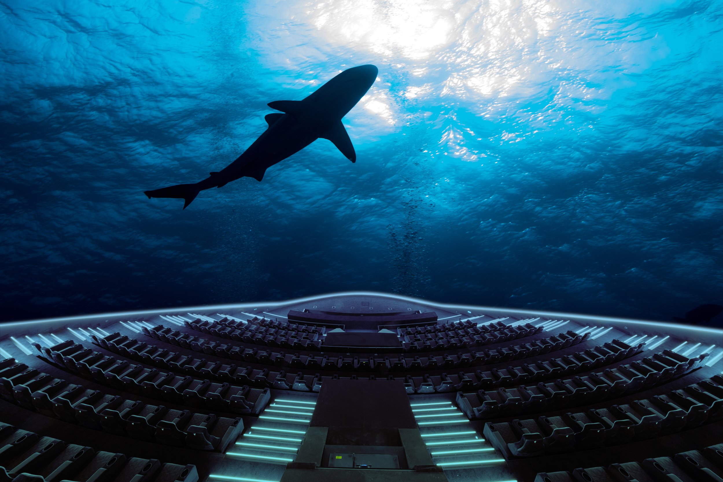 An underwater scene with a large predator shark swimming above an illuminated, empty auditorium or theater with curved seating.