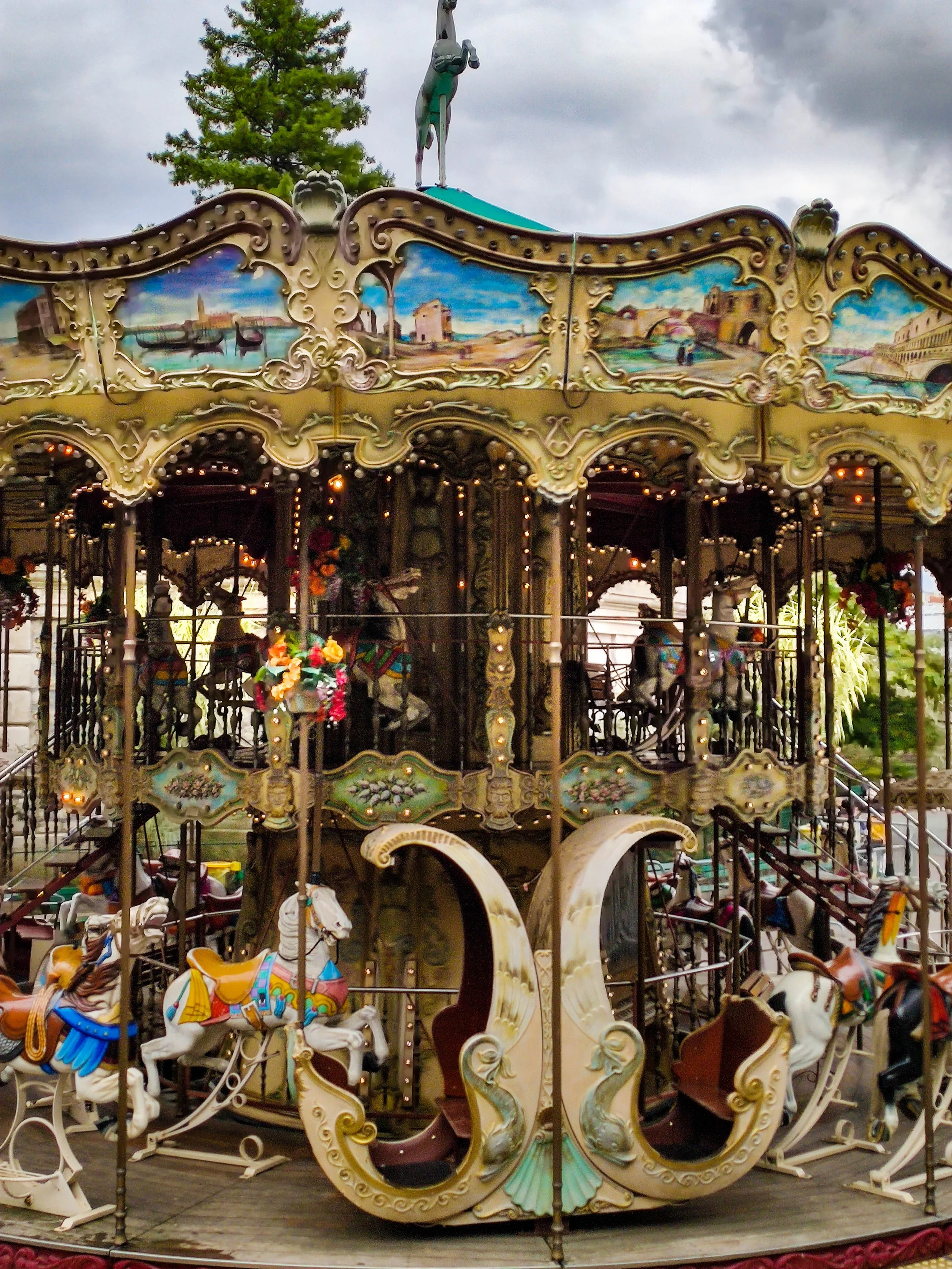 A vintage carousel with painted scenes and carousel horses, topped with a statue of a diver.