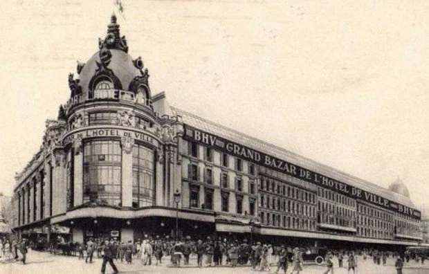 Historical black and white photograph of a large, ornate building with a domed roof, surrounded by people and horse-drawn carriages, with signage indicating it is a hotel in an urban setting.