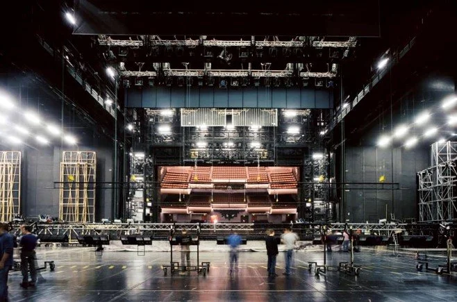 View of a theater stage under construction with crew members working, scaffolding, and lighting setup.