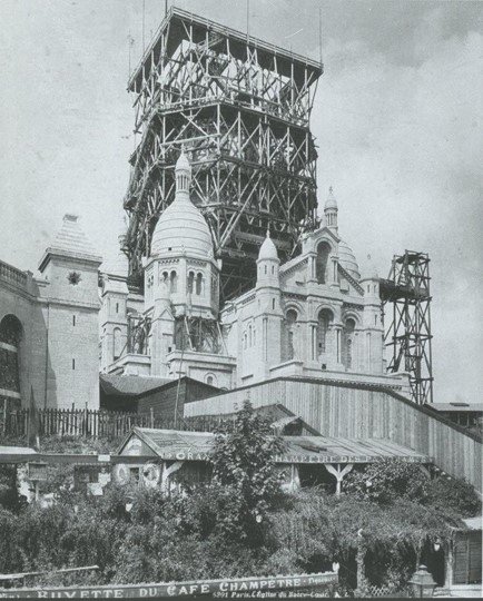 Black and white photo of the construction of a castle or palace, with scaffolding and cranes supporting the structure.