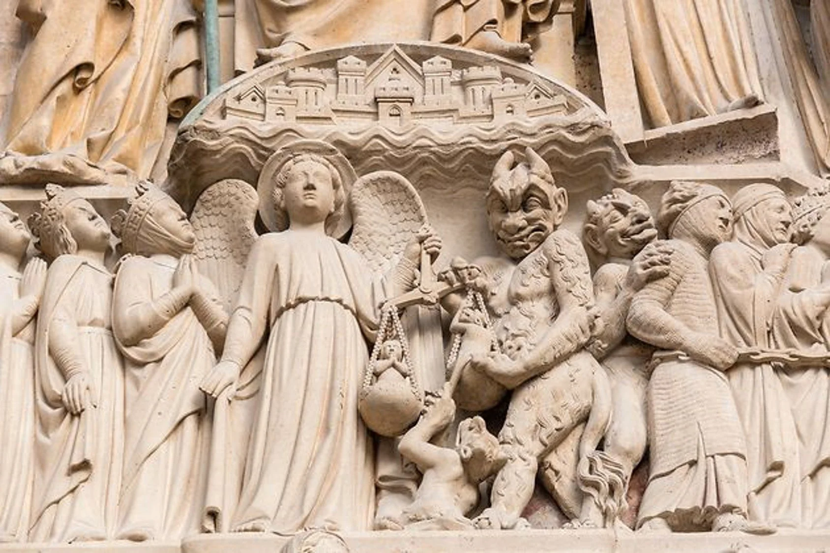 Detailed stone relief sculpture depicting angels, demons, and warriors, with a castle or city above.