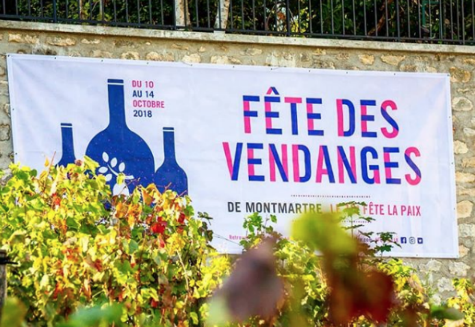 Festival banner for Vendanges (Grape Harvest) event in Montmartre, France, October 2018, with illustrations of wine bottles and grape vines, surrounded by foliage.