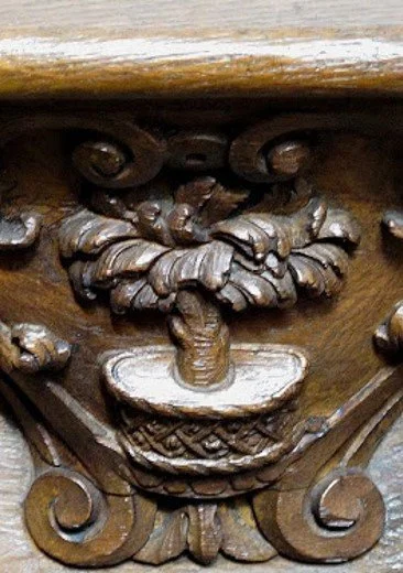 Close-up of a wooden carved design featuring a basket with a flower, surrounded by scrollwork.
