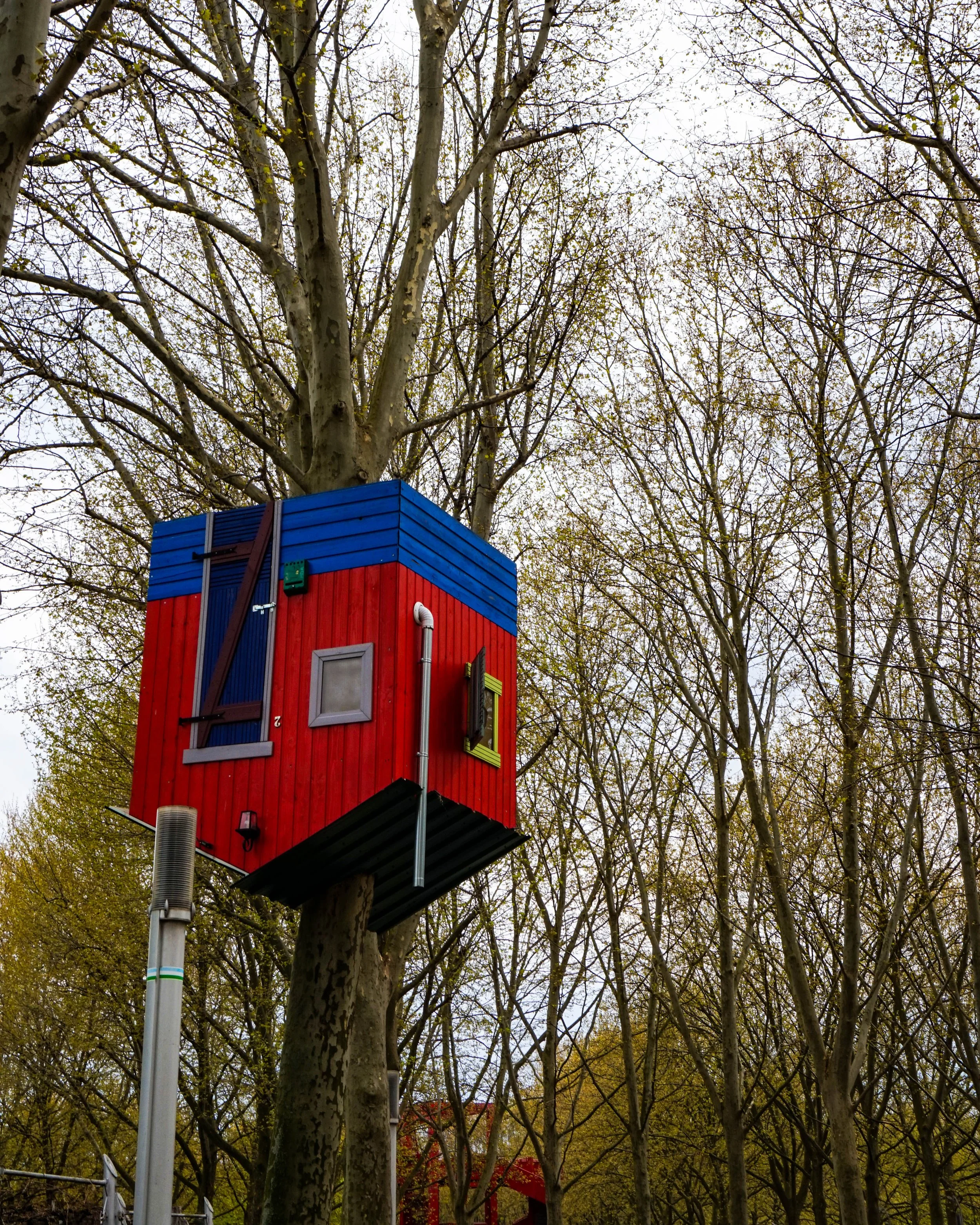 Colorful birdhouse attached to a tree in a wooded area, with a cloudy sky in the background.
