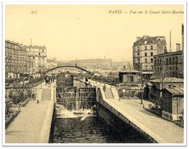 Historical black-and-white photograph of the Saint-Martin Canal in Paris, showing buildings, footbridges, and water locks along the canal with a stone staircase leading to the water.