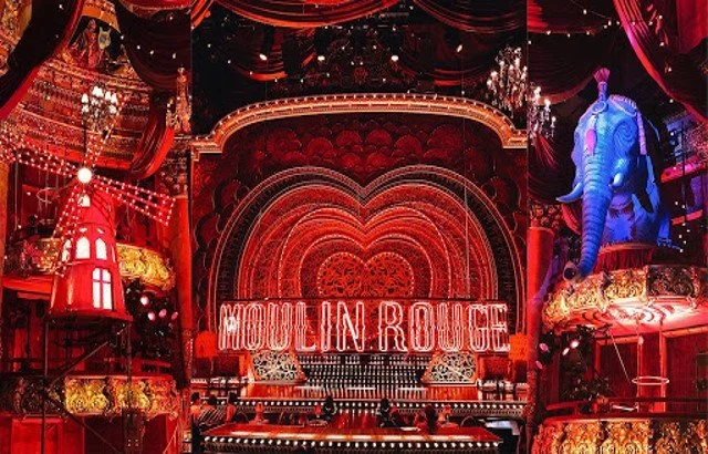 Stage inside the Moulin Rouge with red lighting, a large heart-shaped backdrop, and illuminated sign reading 'Moulin Rouge.' There is a blue elephant figure to the right and ornate gold decor on the sides.