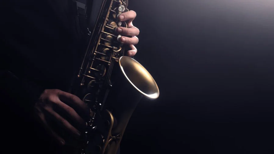 Close-up of a person playing a brass saxophone, with a dark background.