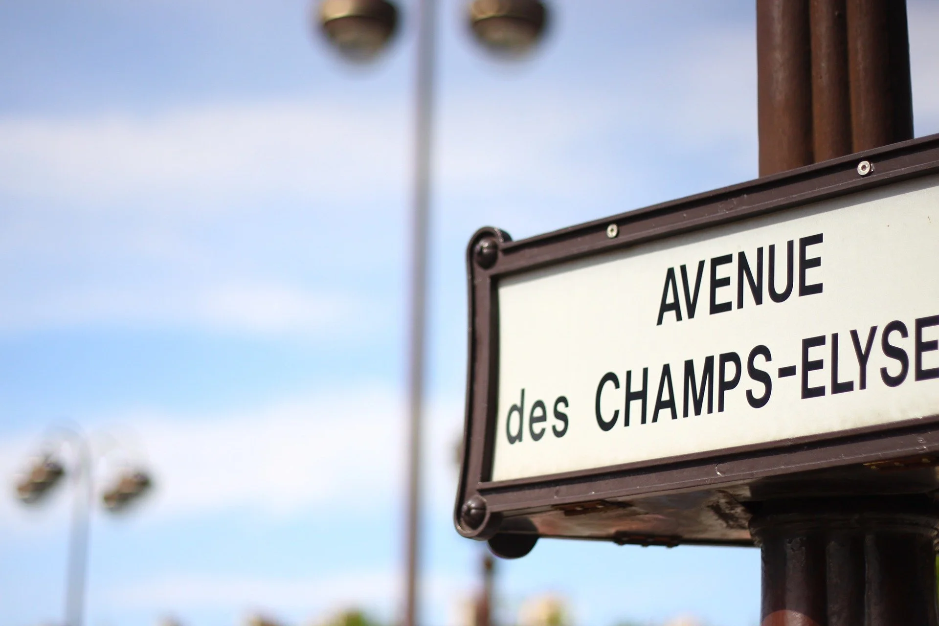 Street sign reading 'Avenue des Champs-Elysees' against a cloudy sky with streetlights in the blurred background.