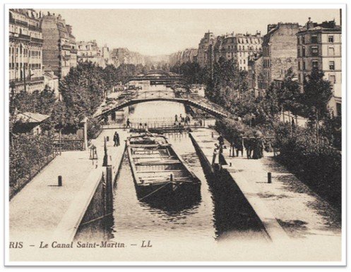 Vintage black-and-white photo of a canal in Paris with a boat, bridges, and historic buildings on both sides.