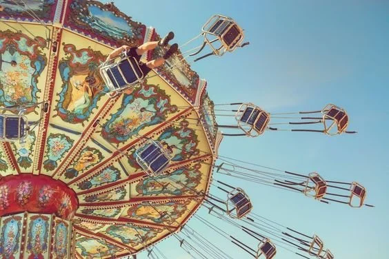 A colorful carnival swing ride with multiple empty swings and a rider enjoying the ride against a clear blue sky.