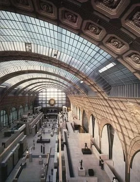 Interior of a large train station with a high arched glass ceiling and ornate architectural details.