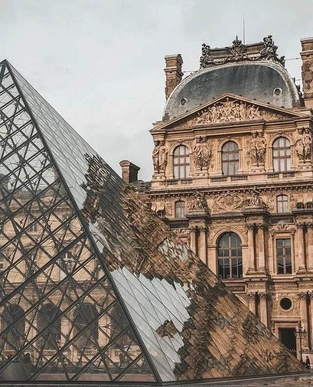 A modern glass pyramid sculpture contrasted with a historic ornate building with sculptures and detailed architecture.