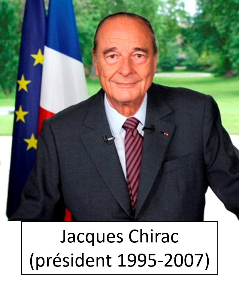 An elderly man in a suit seated at a desk, with a French flag and European Union flag in the background, outdoors with green trees.