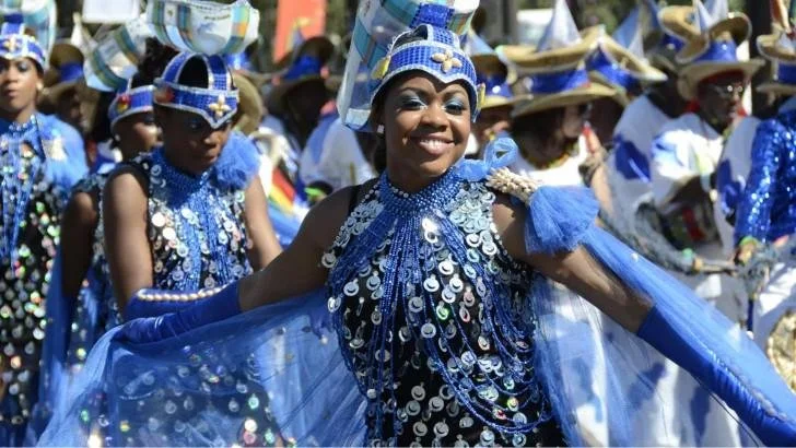 Group of women and children dressed in blue costumes with sequins, beads, and hats participating in a parade or festival.