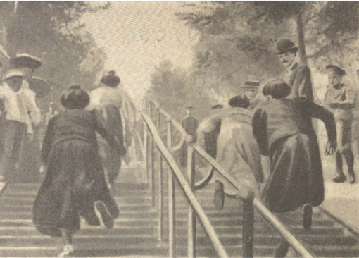 Children climbing stairs outdoors in a park, some wearing hats and dresses, with trees in the background.