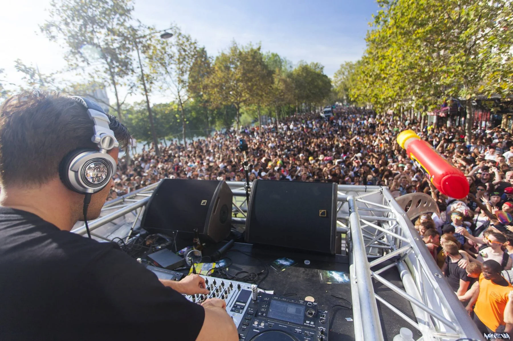 DJ performing at outdoor music event with large crowd and trees in background