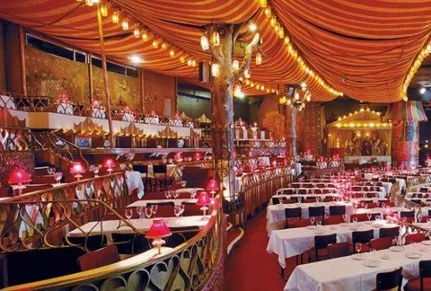 Elegant restaurant decorated with orange drapes, string lights, and pink table lamps.