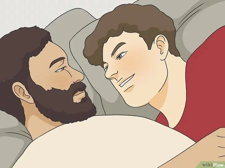 Two men lying close together in bed, making eye contact and smiling at each other.