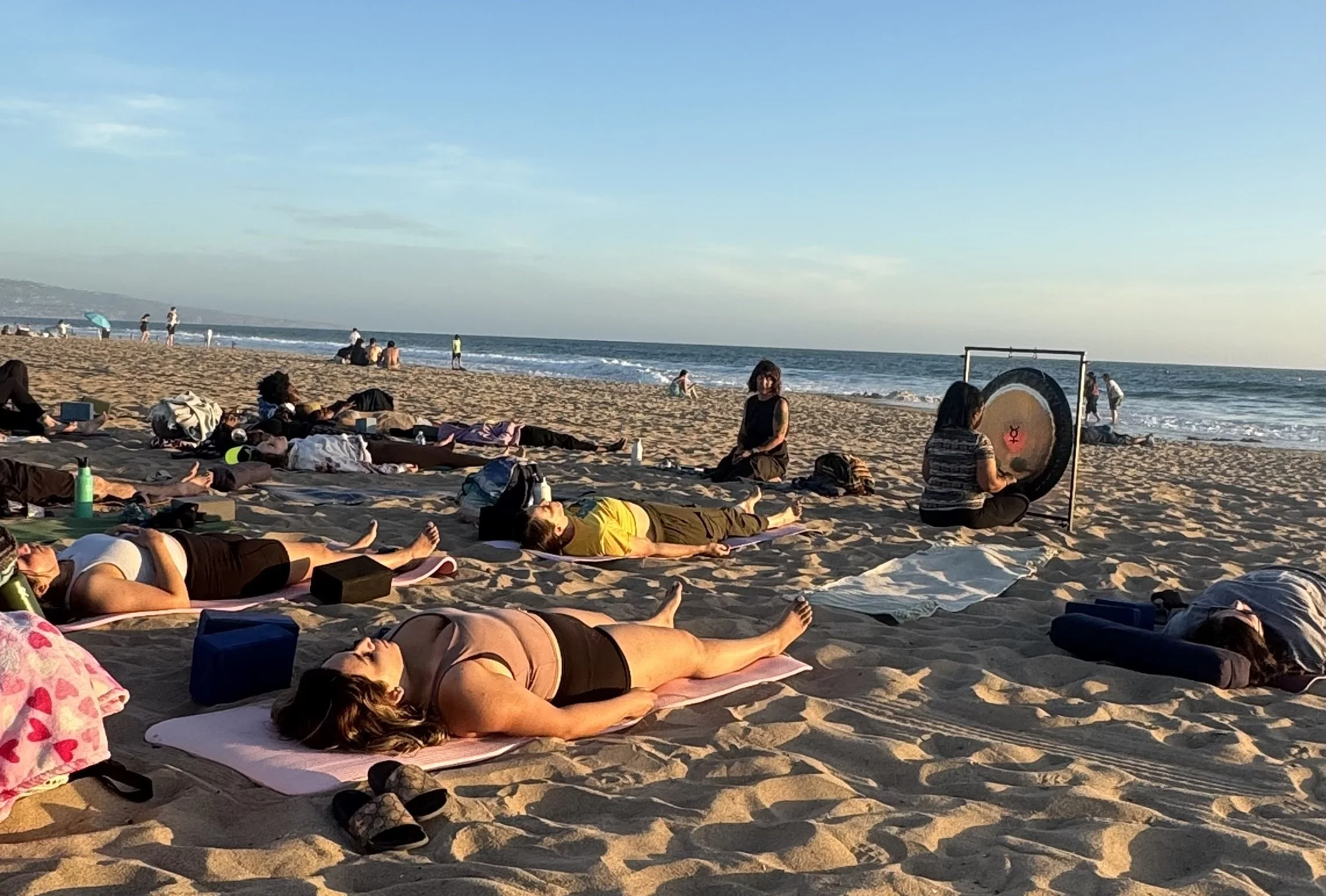 People practicing yoga and relaxing on the beach during sunset with the ocean background.